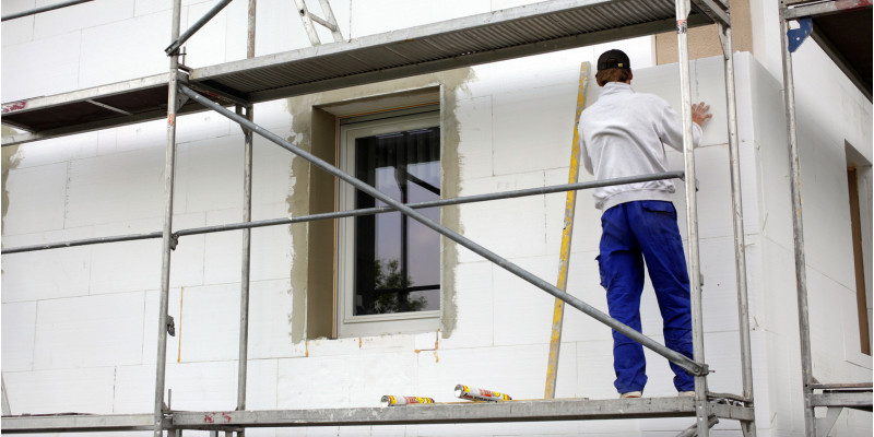 Handwerker steht auf einem Baugerüst und bringt Styroporplatten an eine Hausfassade an