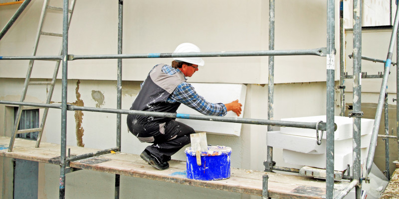 Handwerker auf einem Baugerüst dämmt eine Hausfassade