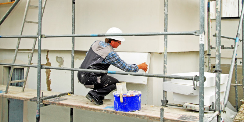 ein Bauarbeiter auf einem Gerüst bringt Dämmplatten aus Polystyrol an einer Hausfassade an