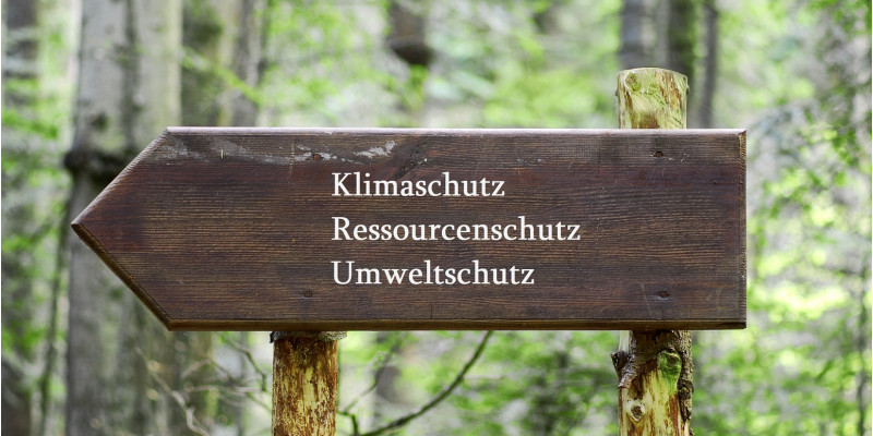 auf einem hölzernen Wegweiser im Wald stehen die Worte Klimaschutz, Ressourcenschutz und Umweltschutz