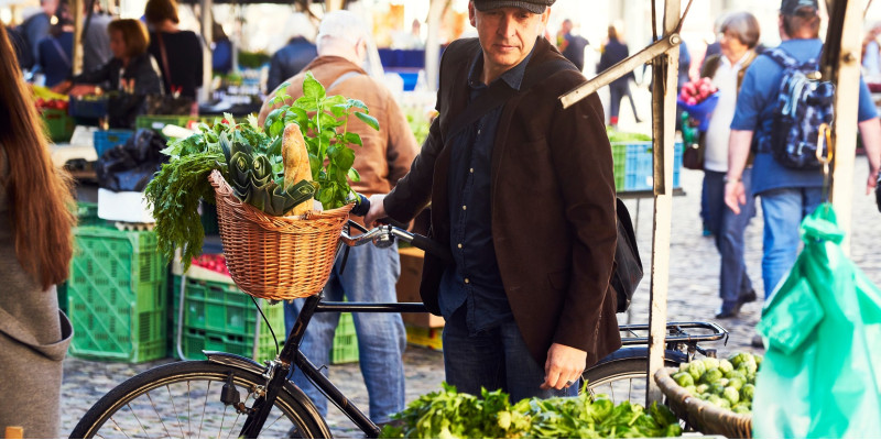 ein Mann kauft mit dem Fahrrad Gemüse auf einem Wochenmarkt ein