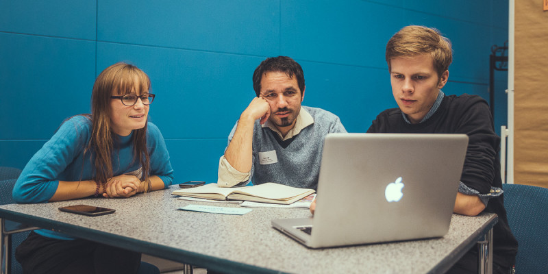 Drei Teilnehmer sehen sich etwas auf einem Laptop an
