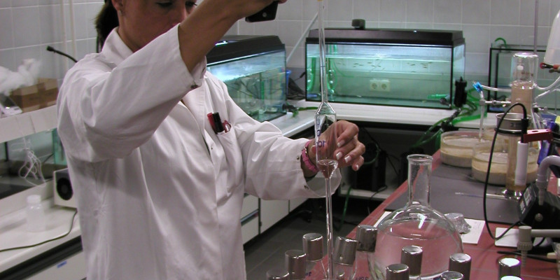 A woman in the apron of the chemistry works in the laboratory. You are filled with liquid glass vessels