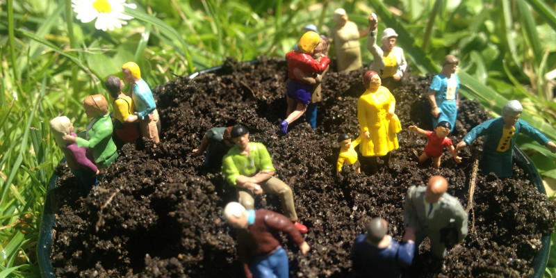 A bucket full of soil on a maedow with various toy figurines