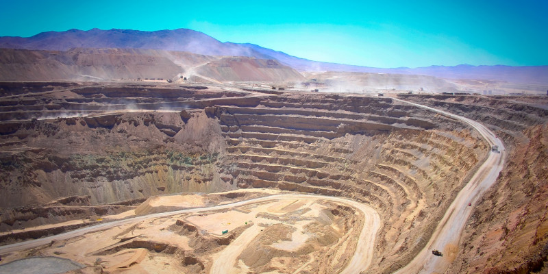 Panoramaufnahme einer Kupfermine: Vorblauen Himmel sieht man die vielen abgetragenen Erdschichten, eine gigantische Kluft.