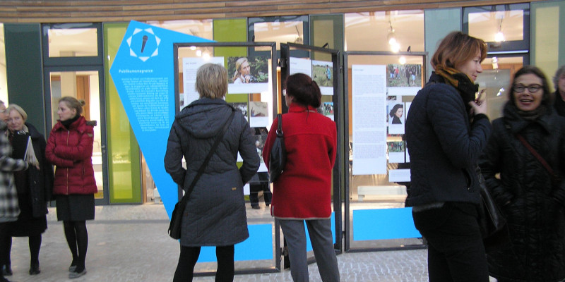 Mehrere Personen schauen sich die Austellung (Schautafeln) im Atrium des Umweltbundesamtes in Dessau an. 