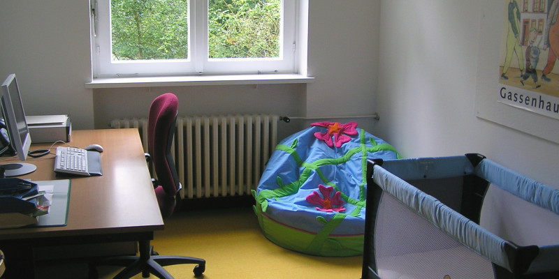 Eltern-Kind-Zimmer: gegenüber vom Schreibtisch steht ein Bett für Kleinkinder, in der Ecke liegt ein bunter Sitzsack