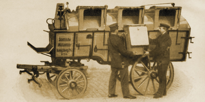 Zwei Arbeiter laden eine Tonne auf einen Wagen