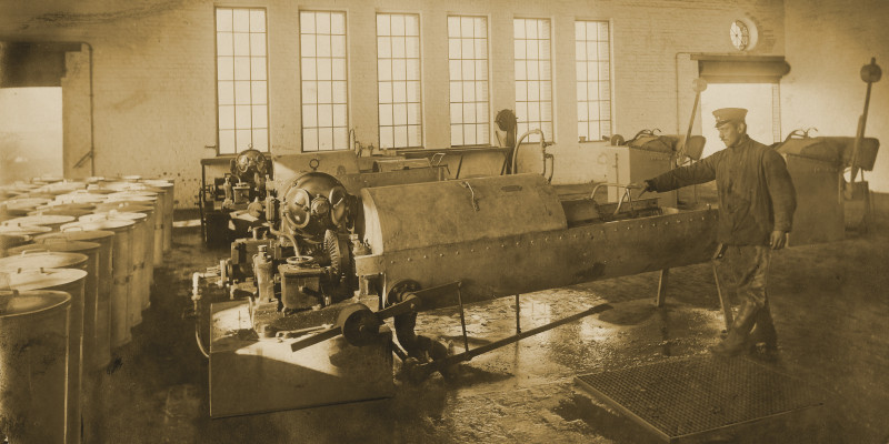 Bürstenwaschmaschine in einem Fabrikgebäude, ein Arbeiter zieht eine Tonne aus der Maschine