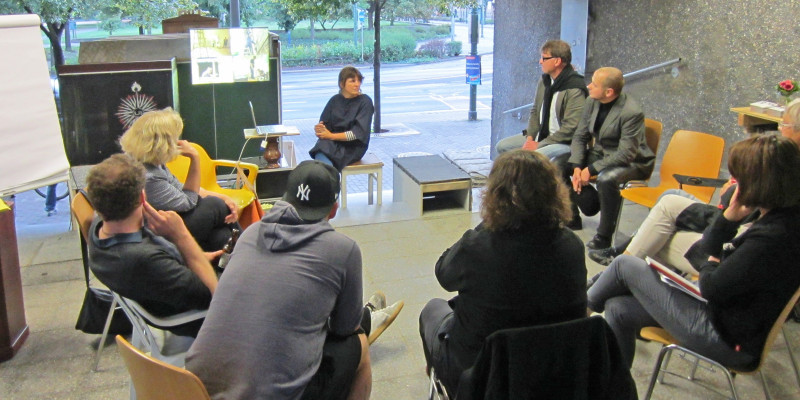 Diskussionsrunde im utopischen Institut: 9 Personen sitzen in einem Stuhlkreis