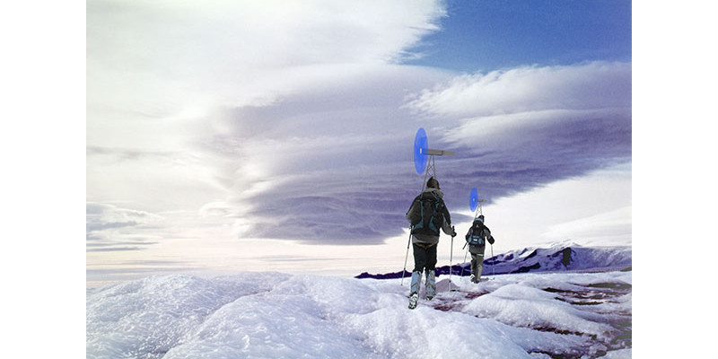 Zwei Bergsteiger laufen auf Schneeschuhen durch eine Eislandschaft, auf dem Rücktragen tragen sie mobile Windräder und erzeugen Strom