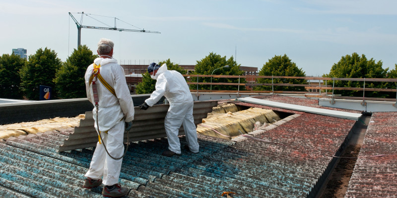 Construction workers in white protective suits and respirators in a corrugated asbestos roof.