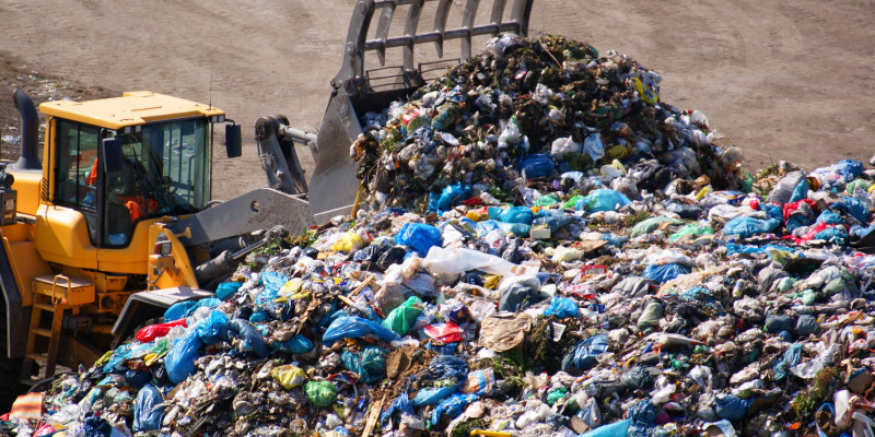 A backhoe pushes together the waste of the waste landfill