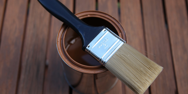 Holzschutz-Farbdose mit brauner Farbe mit einem quer darüber liegenden Pinsel