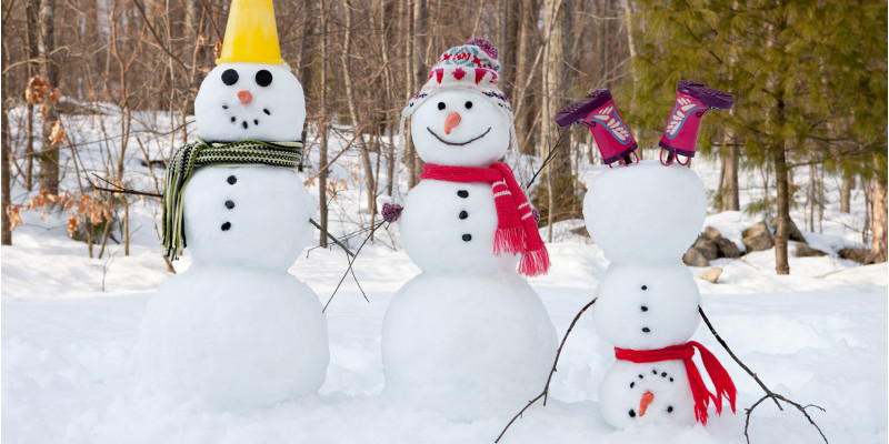 Drei Schneemänner mit Hut und Schal. Einer steht auf dem Kopf und trägt Gummistiefel