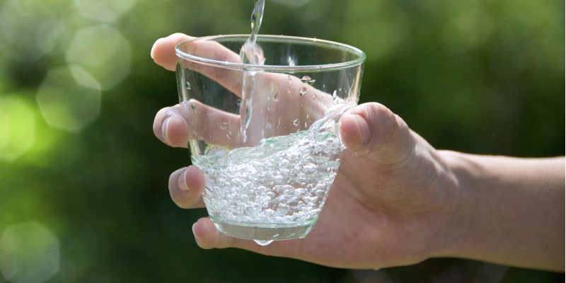 Wasserstrahl trifft von einer Hand gehaltenes Wasserglas