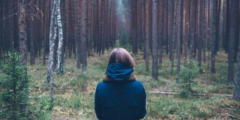 Frau steht mit Rücken zugewandt im Wald.