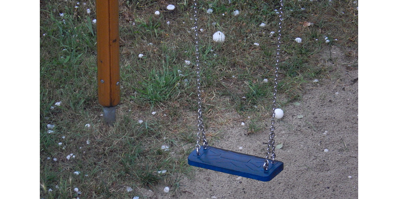 Eine Schaukel blaue Schaukel. Auf dem Boden liegen viele große Hagelkörner.