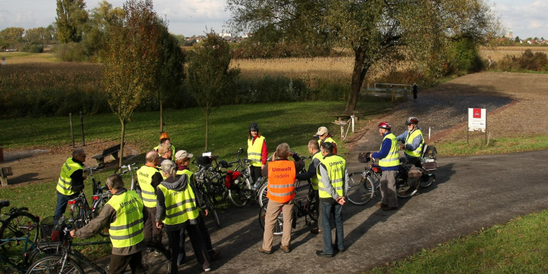 Ein Gruppe von Fahrradfahrerinnen und -fahrern, die alle Westen mit der Aufschrift "Umweltradeln" tragen,  im Feld 