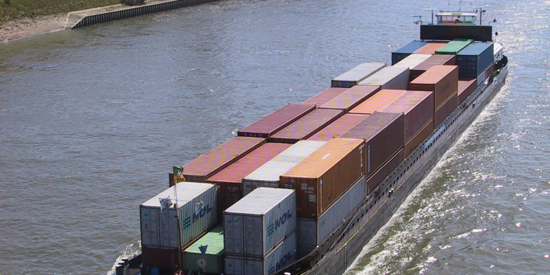 Ein großes Containerschiff fährt bei Sonnenschein auf dem Rhein