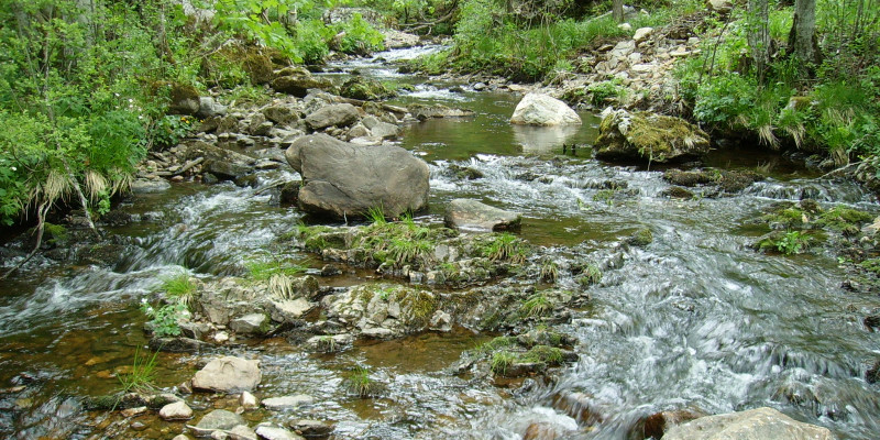 Breiter Bach fließt nach unten, zwischen Geröll und anderen Steinen.