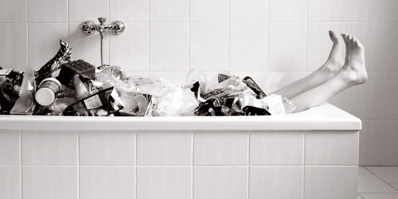 Scharzweiß Foto von einer Badewanne voller Plasikmüll aus der nur noch zwei Beine gucken