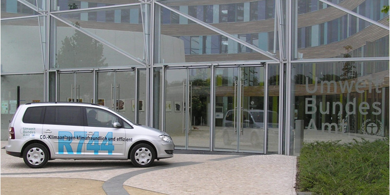Ein silberner VW Touran steht vor Glastüren. Auf dem Auto steht in scharzer Schrift: CO2-Klimaanlagen - klimafreundlich und effizient 