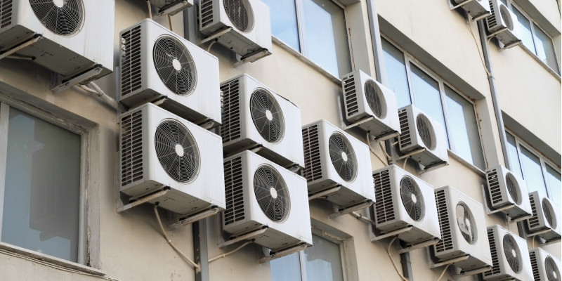 A lot of room air conditioners hangig on the face of a building