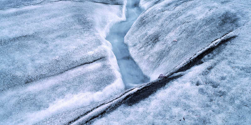 Schmelzwasser läuft eine kleine Rinne entlang.