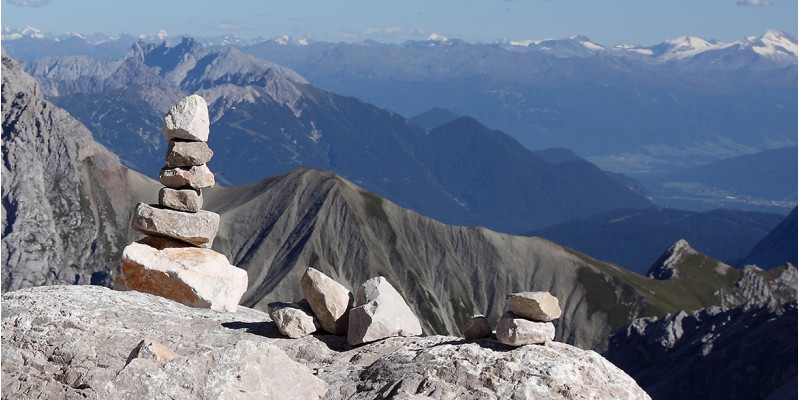 Aufgetürmte Steine im Vordergrund; Panoramablick über die Zugspitze im Hintergrund