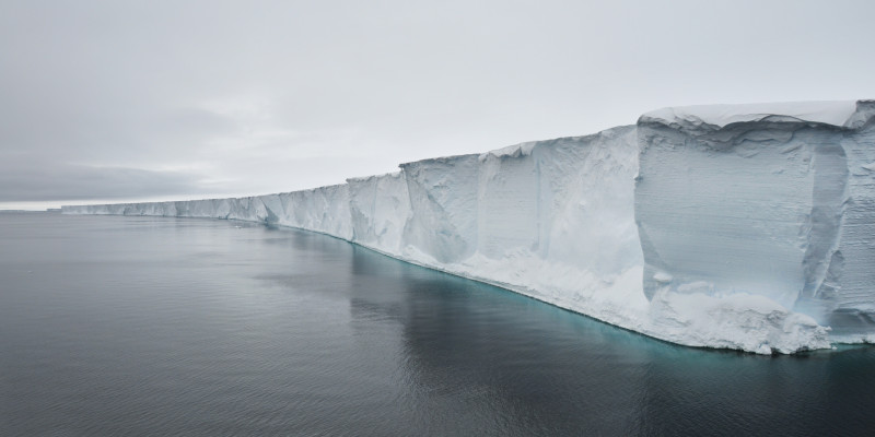 Enormous ice shelves float on the ocean, connected to a glacier onshore.