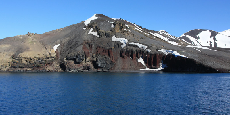 im Vordergrund des Bildes sieht man ruhiges antarktisches Meer vor einem Berg.