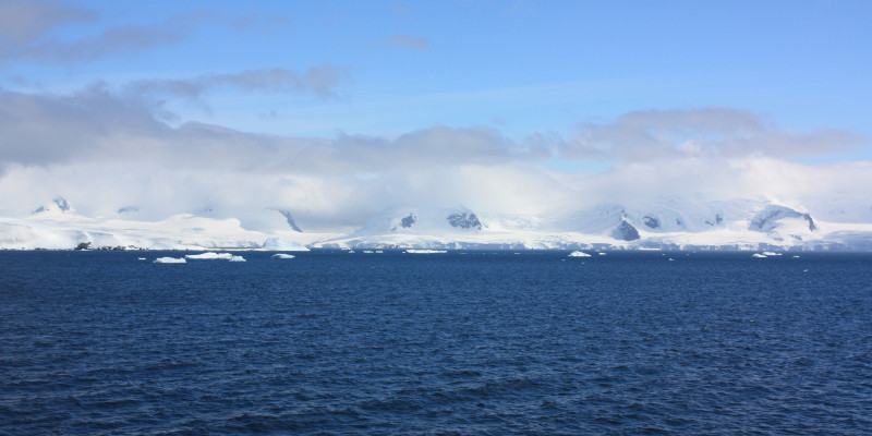Eine weiße Wolkenschicht umgibt antarktische Berge an der Küste. Darüber sieht man eine zweite dunkler und dünnere Wolkenschicht. 