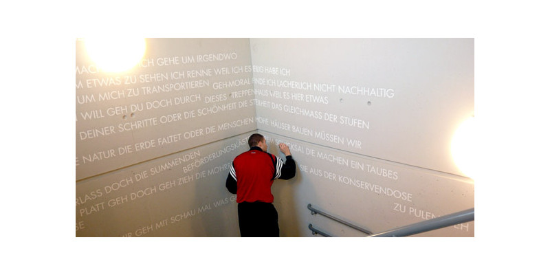 Ein Mann schreibt mittels besagter Schablonen weitere Begriffe und Worte mit weißer Farbe an die Betonwand