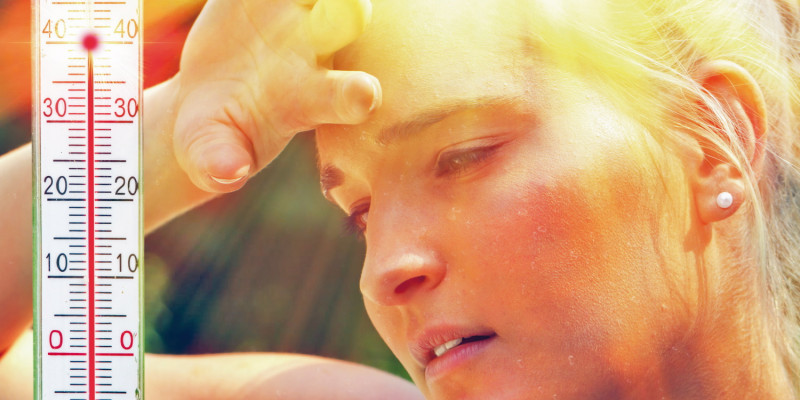 Das Bild zeigt das Gesicht einer Frau mit Schweißperlen in der Sommerhitze. Die frau hält die hand an die Stirn. Links im Bild ist ein Thermometer abgebildet, das 40 Grad Celsuis Lufttemperatur anzeigt.