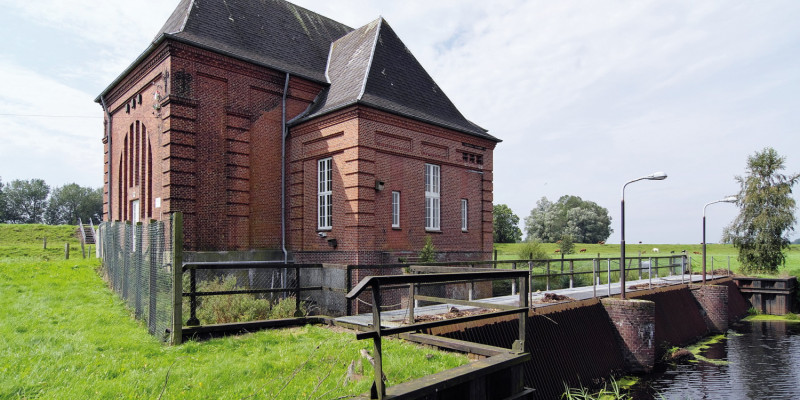 Das Bild zeigt das Schöpfwerk Steinschleuse an der Eider. Es sind eine Staumauer mit Brücke und ein Backsteinhaus zu sehen.