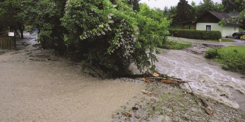 The picture shows a housing estate with a single-family house. A mudslide is pouring over the street in front of it.