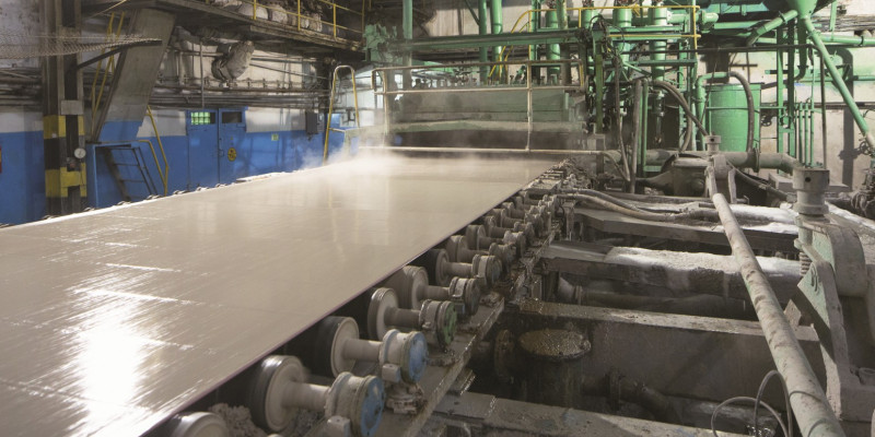 The picture shows a machine on which a wet and steaming strip of paper is pulled over a conveyor belt.