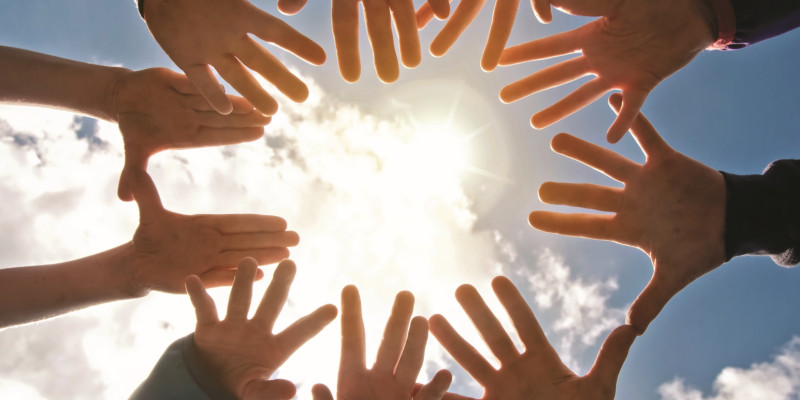 The image is directed towards the sky against the sun and shows a circle of ten stretched hands in a circle.