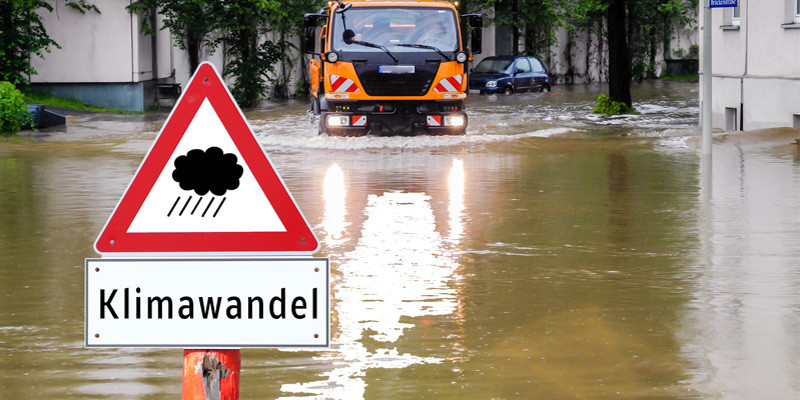 von Starkregen überflutete Straße mit Warnschild "Klimawandel"