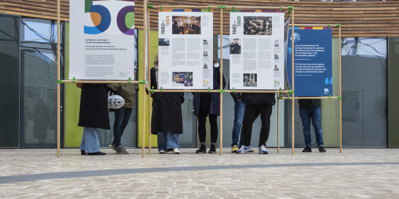 Foto mit den neuen UBA-Ausstellungstalfen in Dessau-Roßlau. Zu sehen ist ein Teil der Ausstellung mit Menschen hinter den Tafeln. 