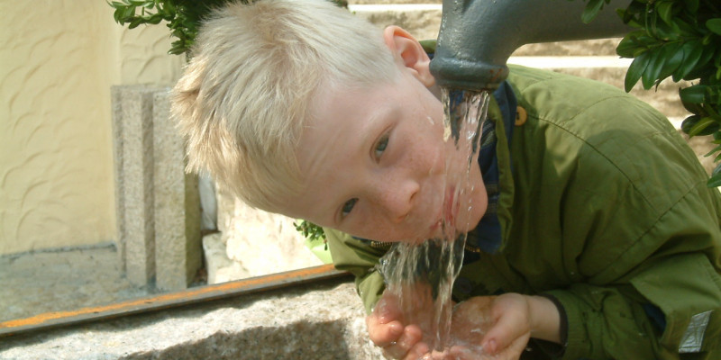 Ein Junge, der aus einem Hahn in der Stadt Trinkwasser trinkt. 