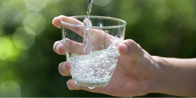 Zu sehen ist eine Hand, die ein Glas hält, in das Wasser gegossen wird. 