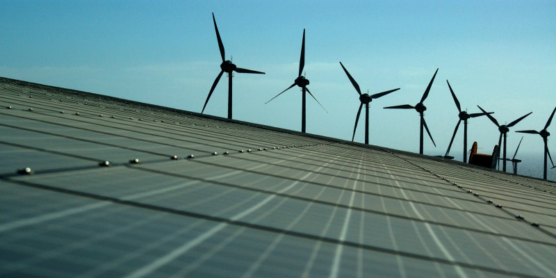 Eine Solaranlage auf freien Feld, im Hintergrund drehen sich Windkrafträder