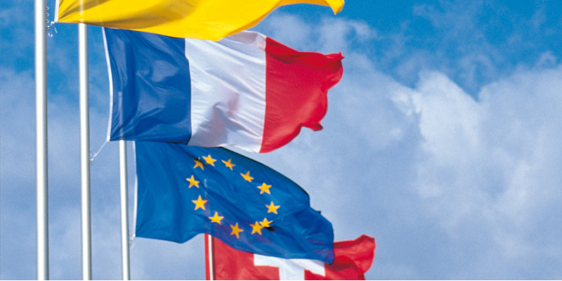 Wehende Flaggen in einer Reihe von vorn nach hinten: Badische Flagge, Frankreich, Europa und Schweiz vor einem blauen Himmel