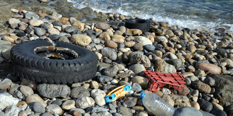 Plastikreste am Meer: Ein alter Reifen, eine Flasche, Kinderspielzeug und der Rest eines Einkaufkorbs aus Plastik liegen auf einem Kiesstrand.