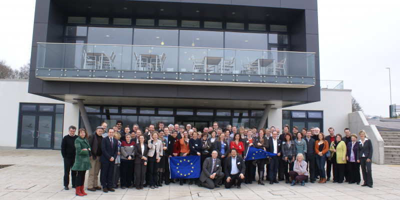 Personengruppe mit EU-Fahne im Hintergrund ein Haus