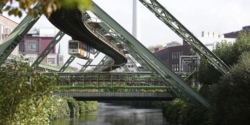 Schwebebahn fährt über einen Fluss, rundum ist Stahlkonstruktion zu sehen.