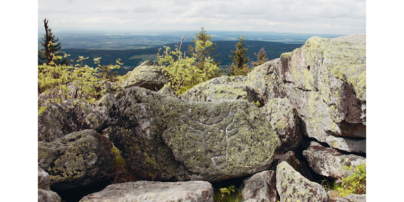 Aufgeschichtetes Felsengestein auf dem Ochsenkopf gibt einen Blick frei über das Fichtelgebirge. In der Ferne ist der Horizont sichtbar.