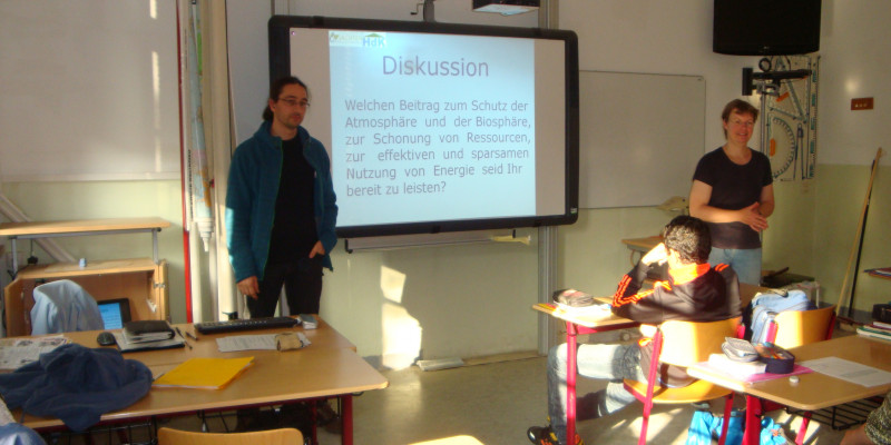 Zwei Seminarleiter stehen vorne im Klassenraum und diskutieren mit der Klasse.